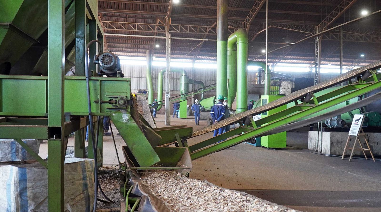 Biomass feedstock moving along conveyors inside a biochar production facility