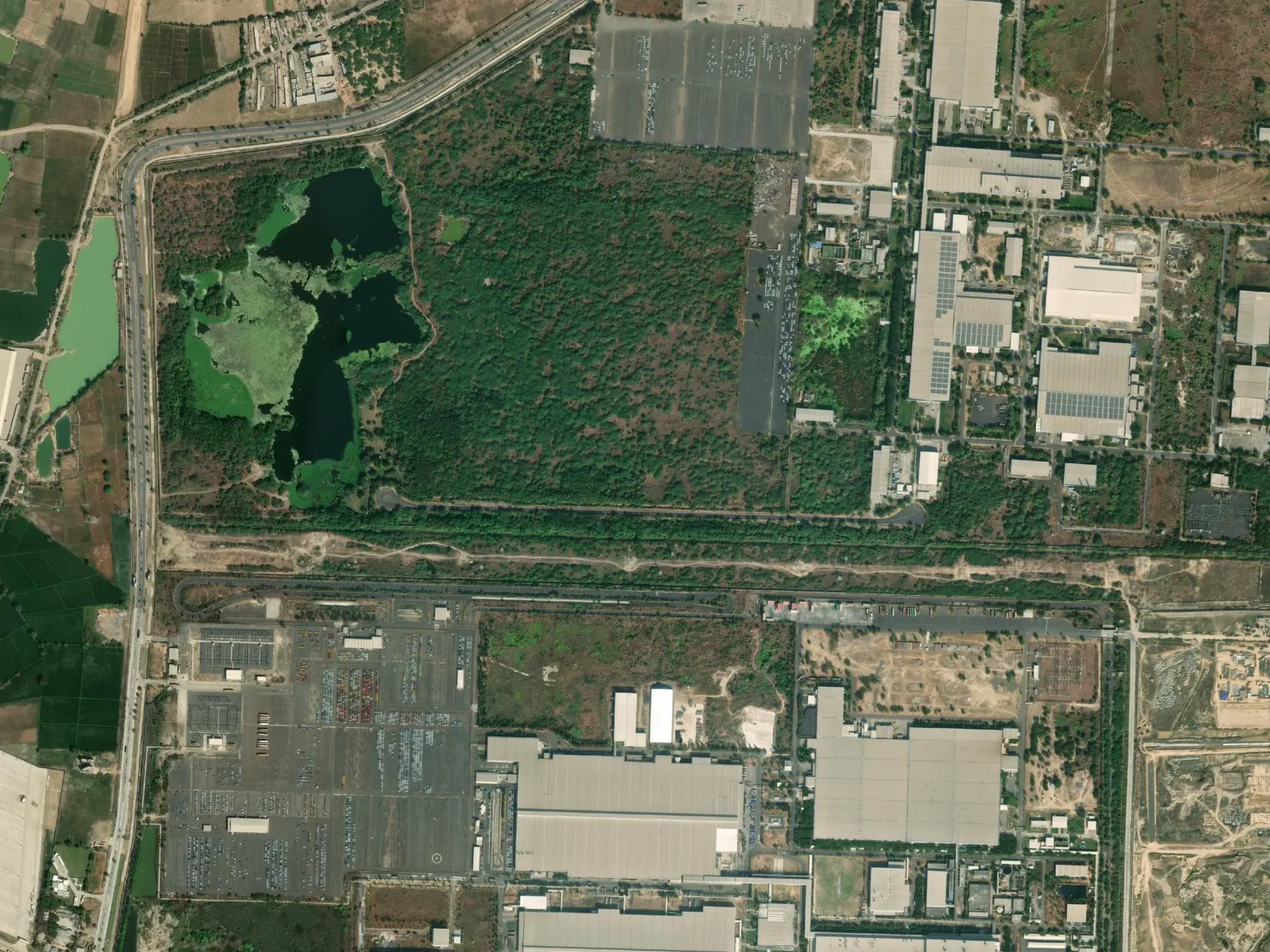 The same site in December 2025, with dense tree cover around the lake beside the factory